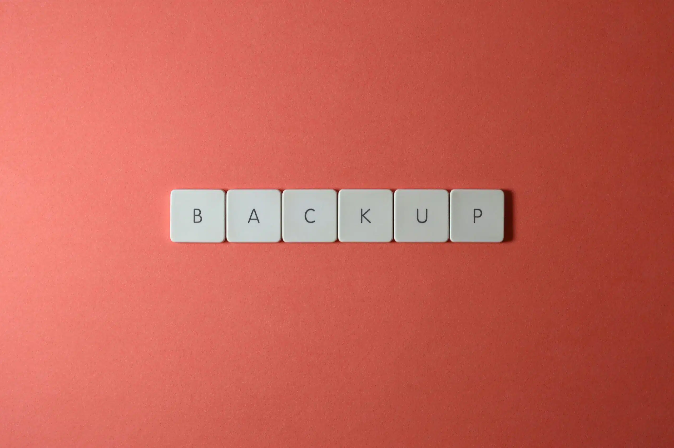 Free Close-up of keyboard keys spelling 'BACKUP' placed on a coral-colored surface. Stock Photo